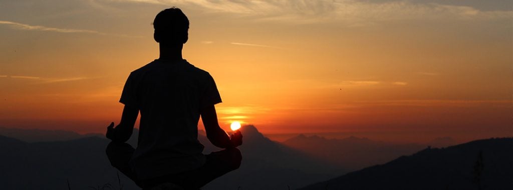 silhouette of a man meditating in front of a sunset